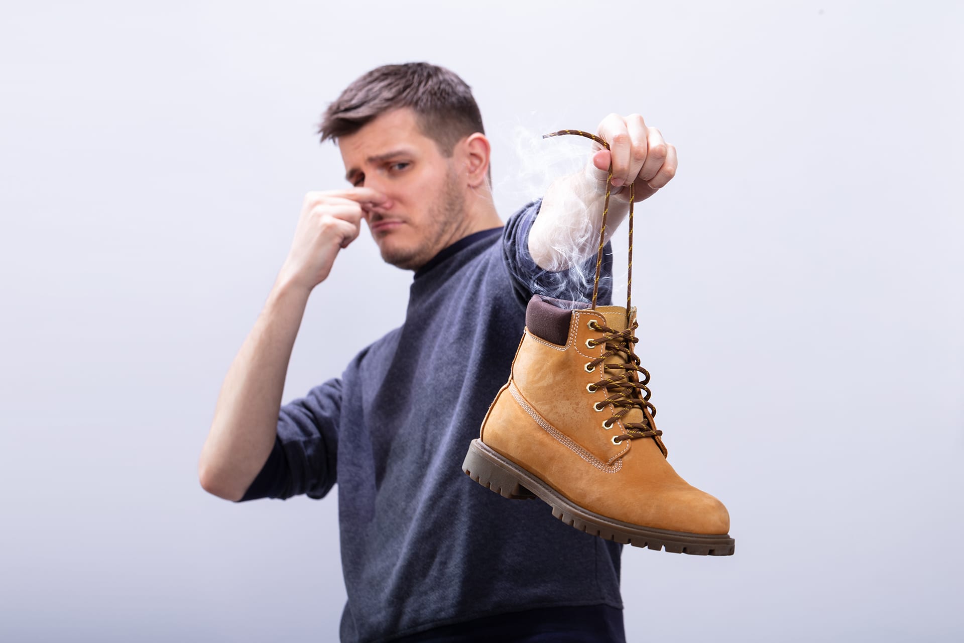 Man Covering His Nose While Holding Stinky Shoe